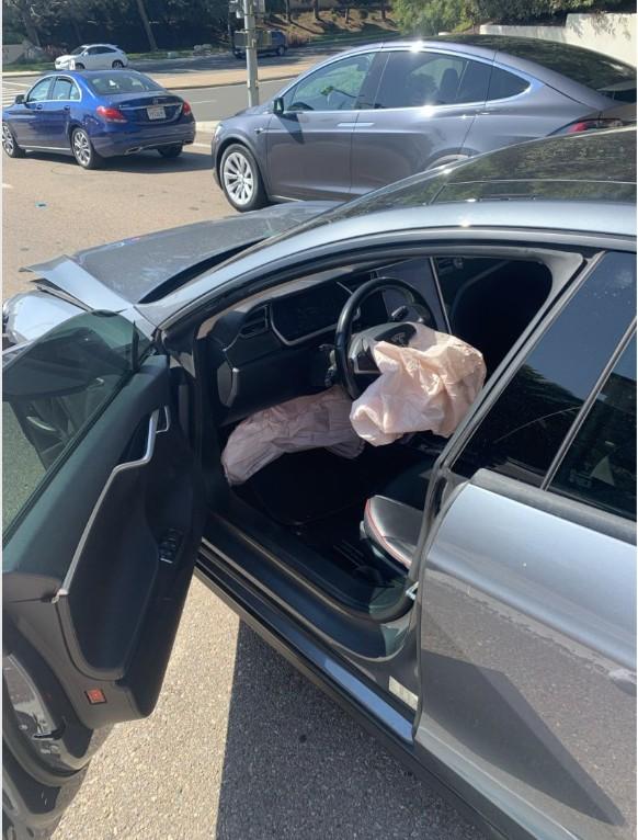 The interior of Wayne Partello's Tesla after a car accident, showing a deployed airbag and the driver's door open.