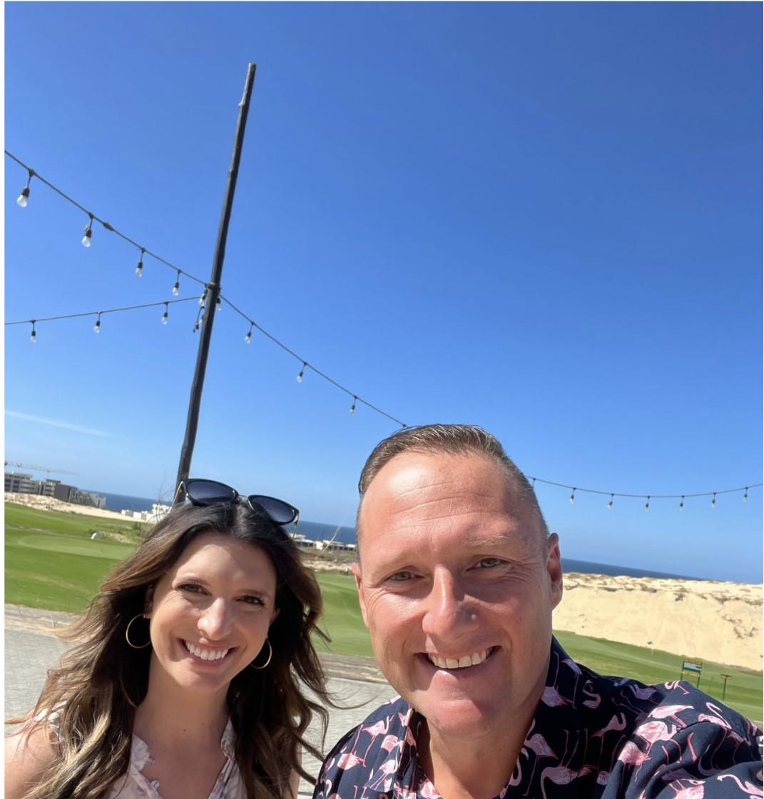 Wayne Partello takes a selfie with a companion on a golf course overlooking the ocean, wearing his flamingo-print shirt.