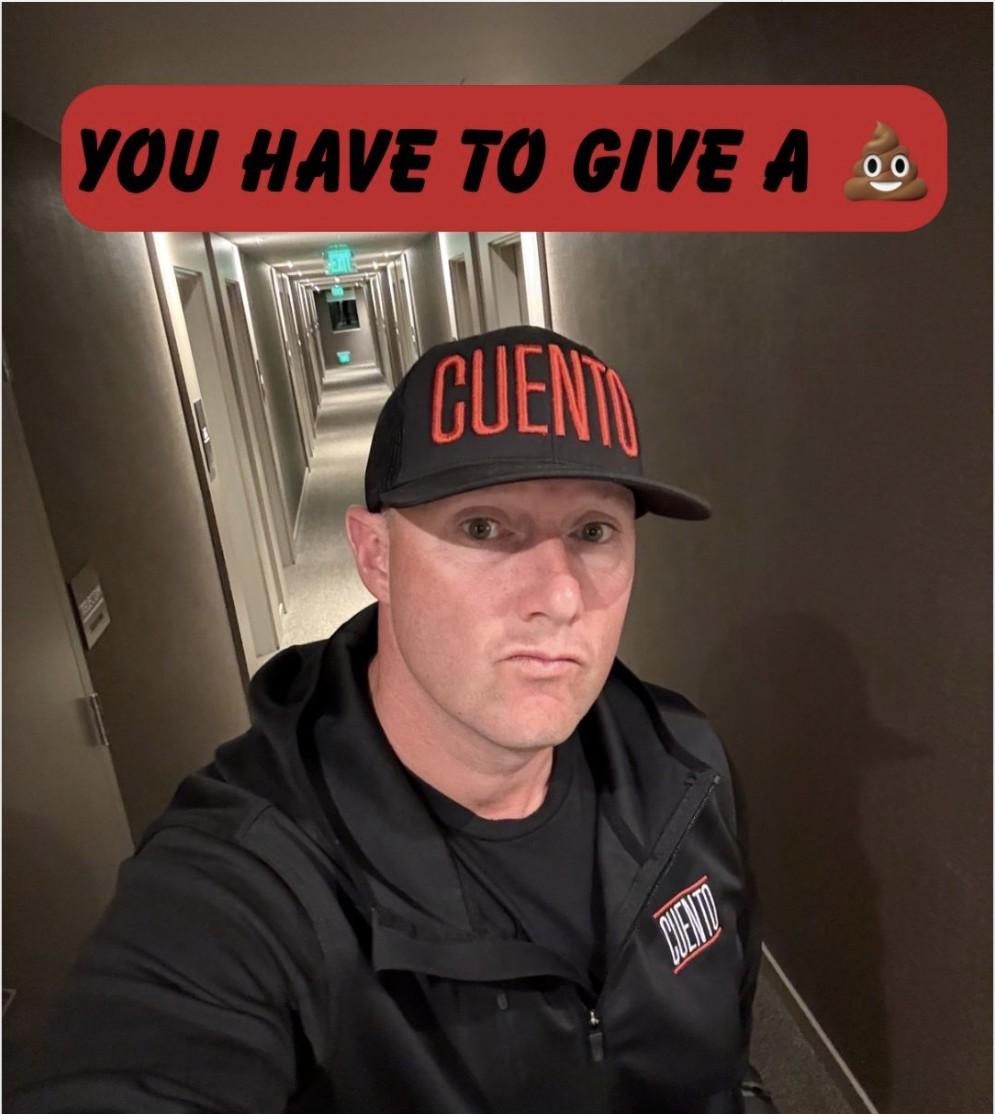 Selfie of Wayne Partello wearing a CUENTO trucker hat and jacket in a hotel hallway, with bold text reading 'You Have to Give a 💩'