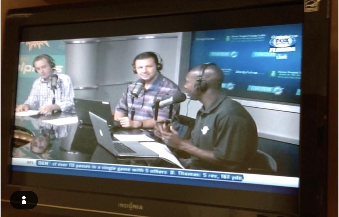 A TV screen showing three broadcasters recording The Finsiders show on Fox Sports Florida, with Miami Dolphins branding on set.