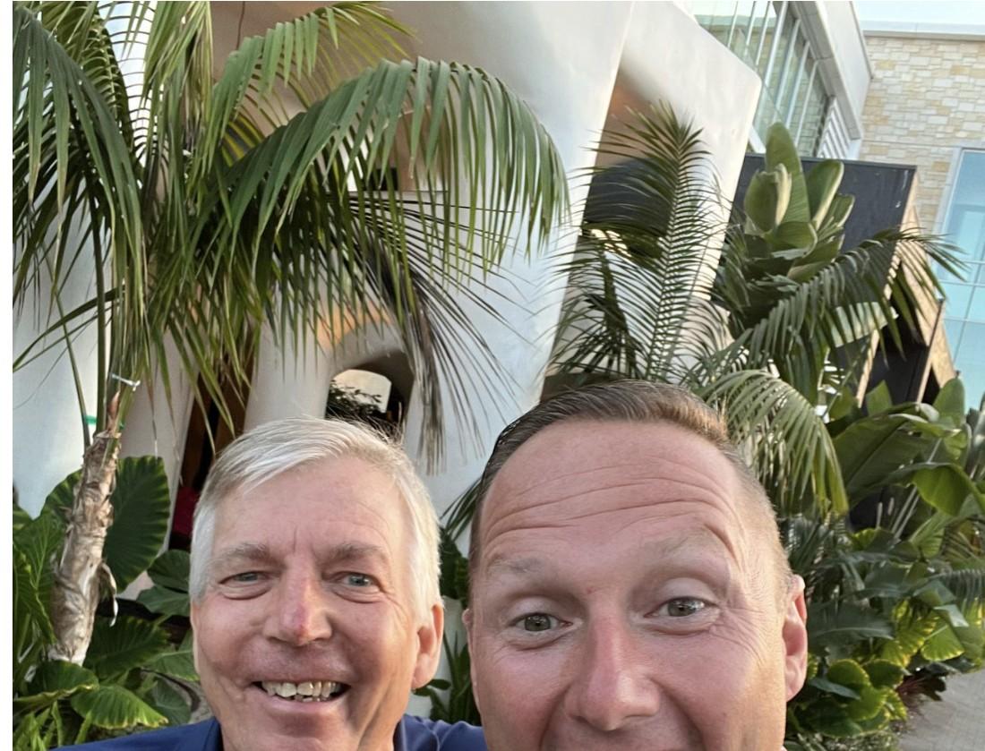 Wayne Partello and his friend Bob Bolinger smiling in a selfie surrounded by palm trees.