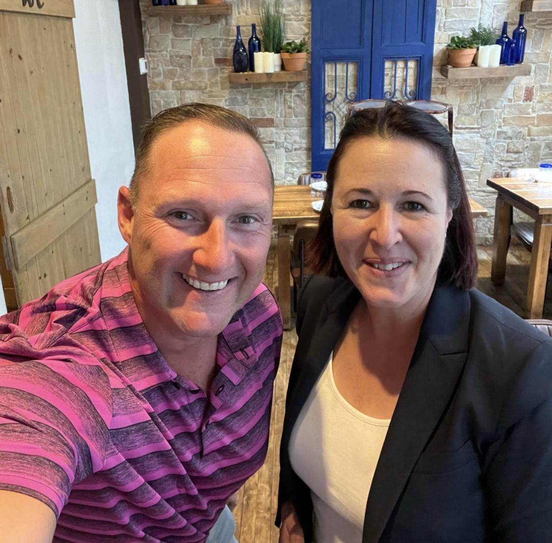 Wayne Partello takes a selfie with a former colleague indoors.