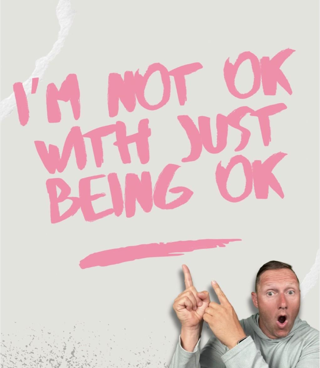 Wayne Partello points at hand-lettered pink text reading "I'm not OK with just being OK."