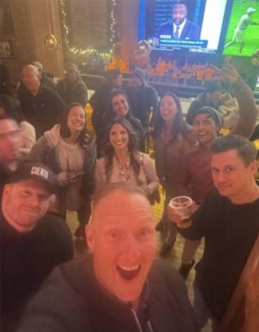 Wayne Partello takes a group selfie with the CUENTO team at a bar, wearing a CUENTO cap.