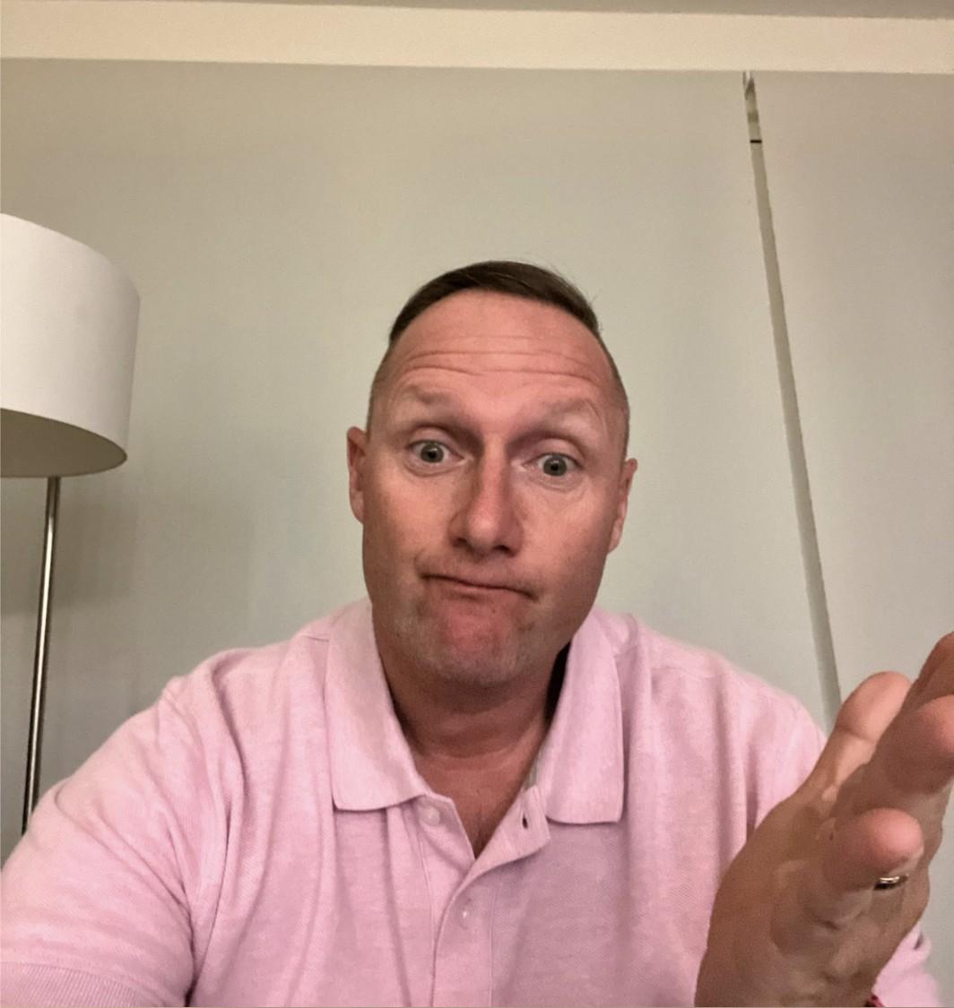 Wayne making an exaggerated shrugging expression in a casual selfie at home, gesturing with one hand.