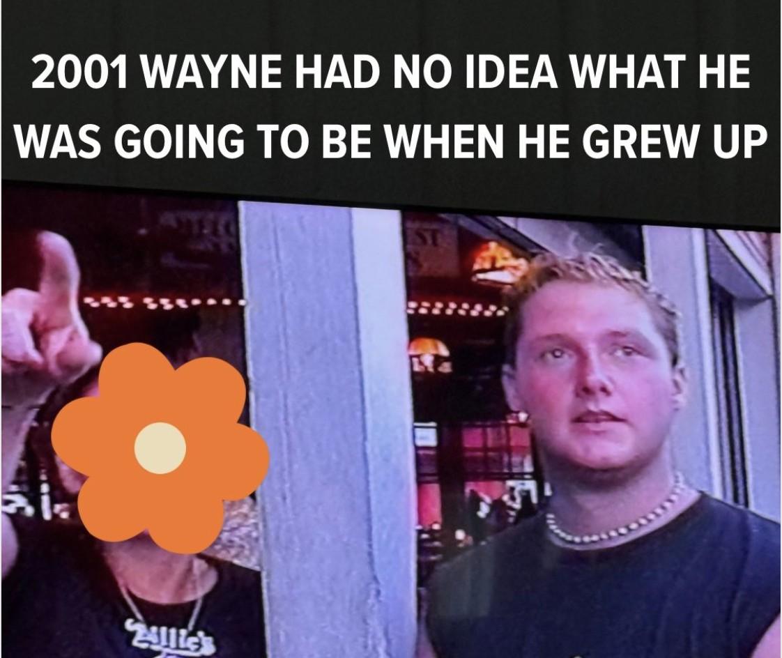 A young Wayne Partello in 2001 standing outside a bar in Key West, Florida, with a companion whose face is covered by a decorative orange flower sticker, captioned '2001 Wayne had no idea what he was going to be when he grew up'