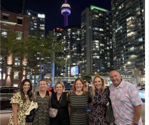 Group photo of six people standing outdoors at night in downtown Toronto with the CN Tower lit up behind them