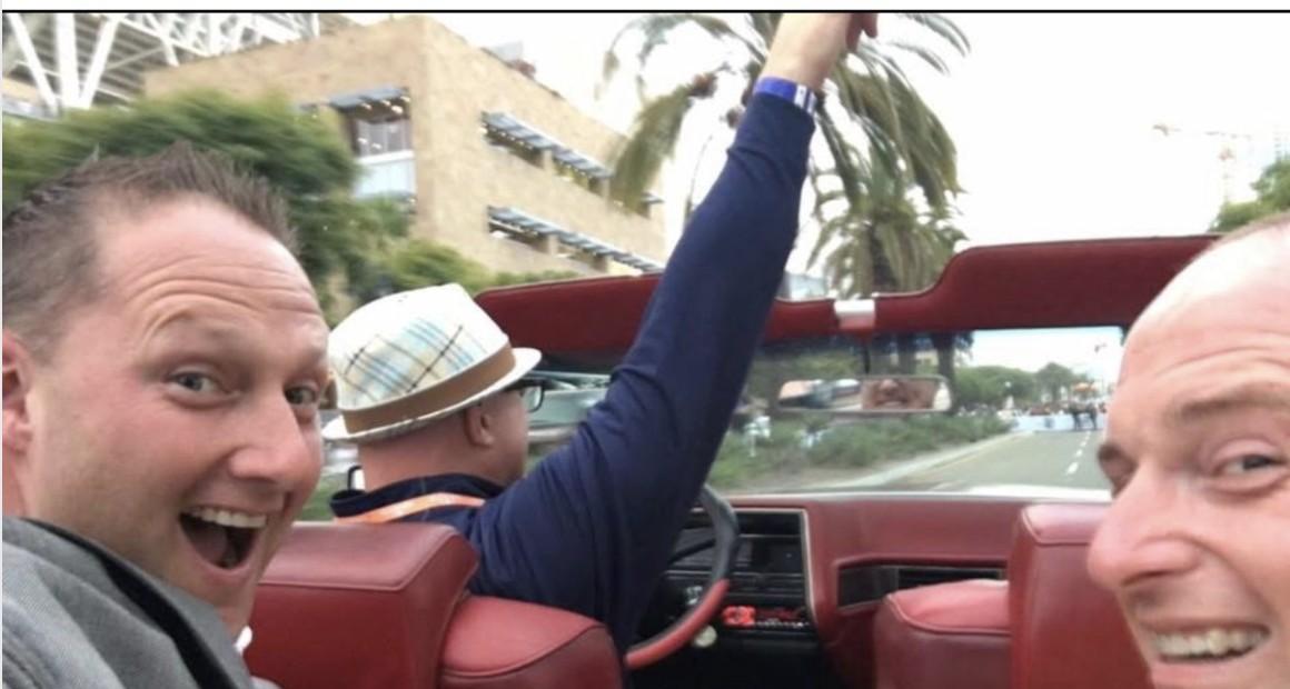 Wayne Partello and two friends laughing in the back seat of a classic red convertible, taken during MLB All-Star week.